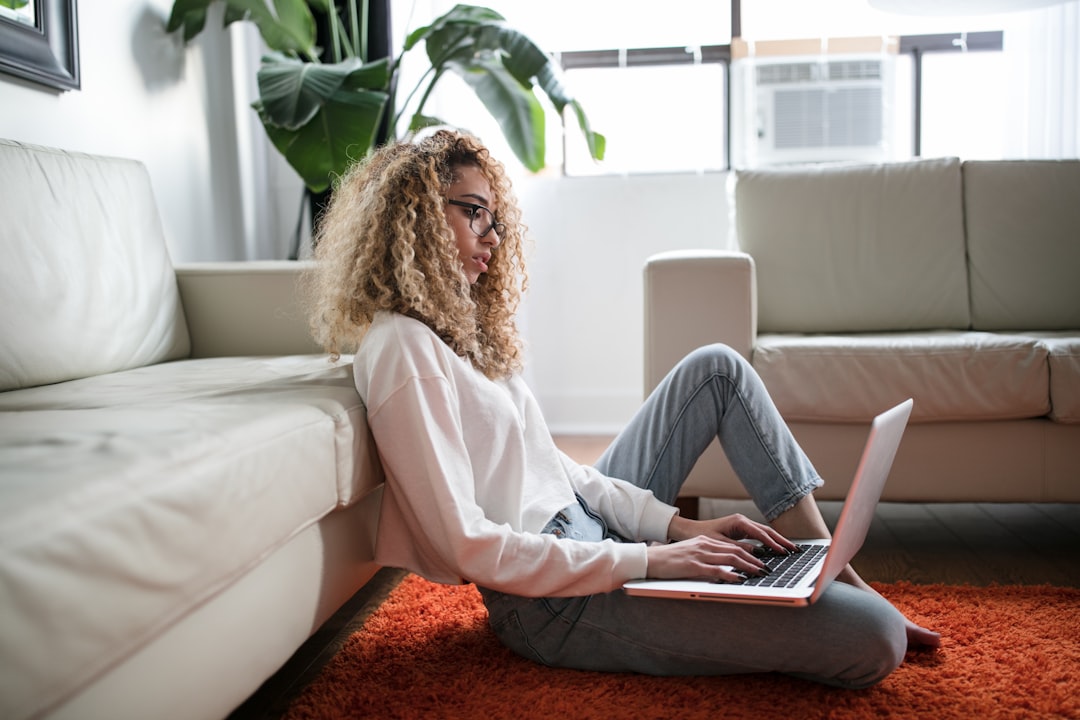 A buyer reading property listings on a laptop and noting down questions about each house