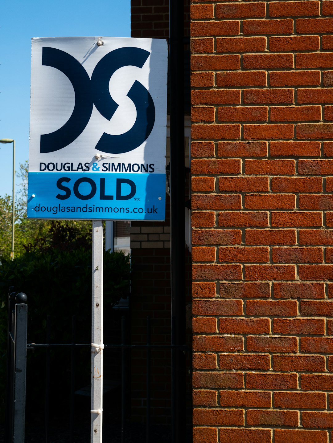 Buyer on the phone to an estate agent outside a terraced house with a for-sale board, asking for the property to be taken off the market
